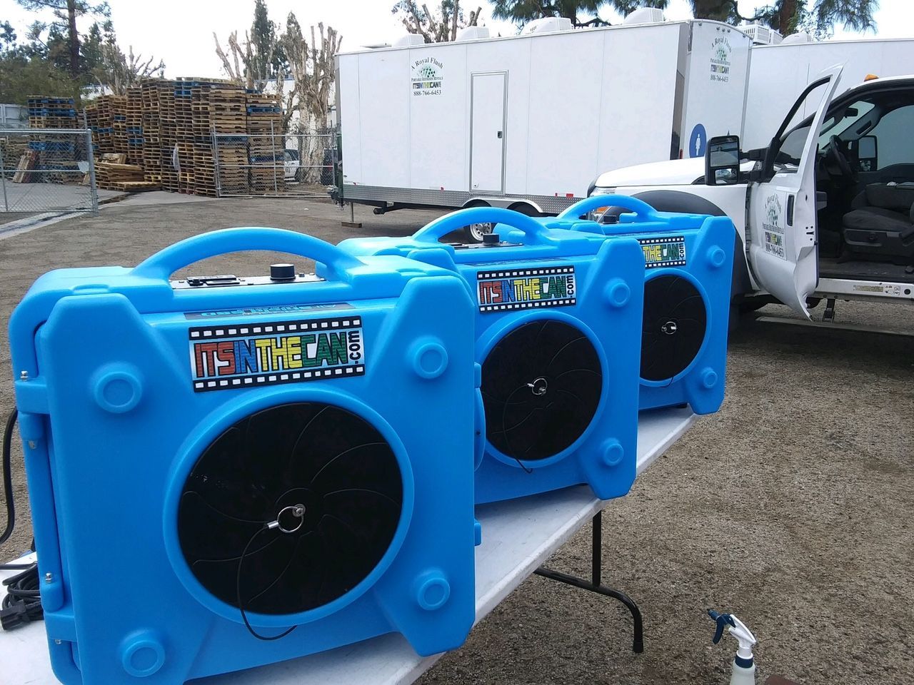 Three blue air movers on a white table; a white truck and trailer are behind them.