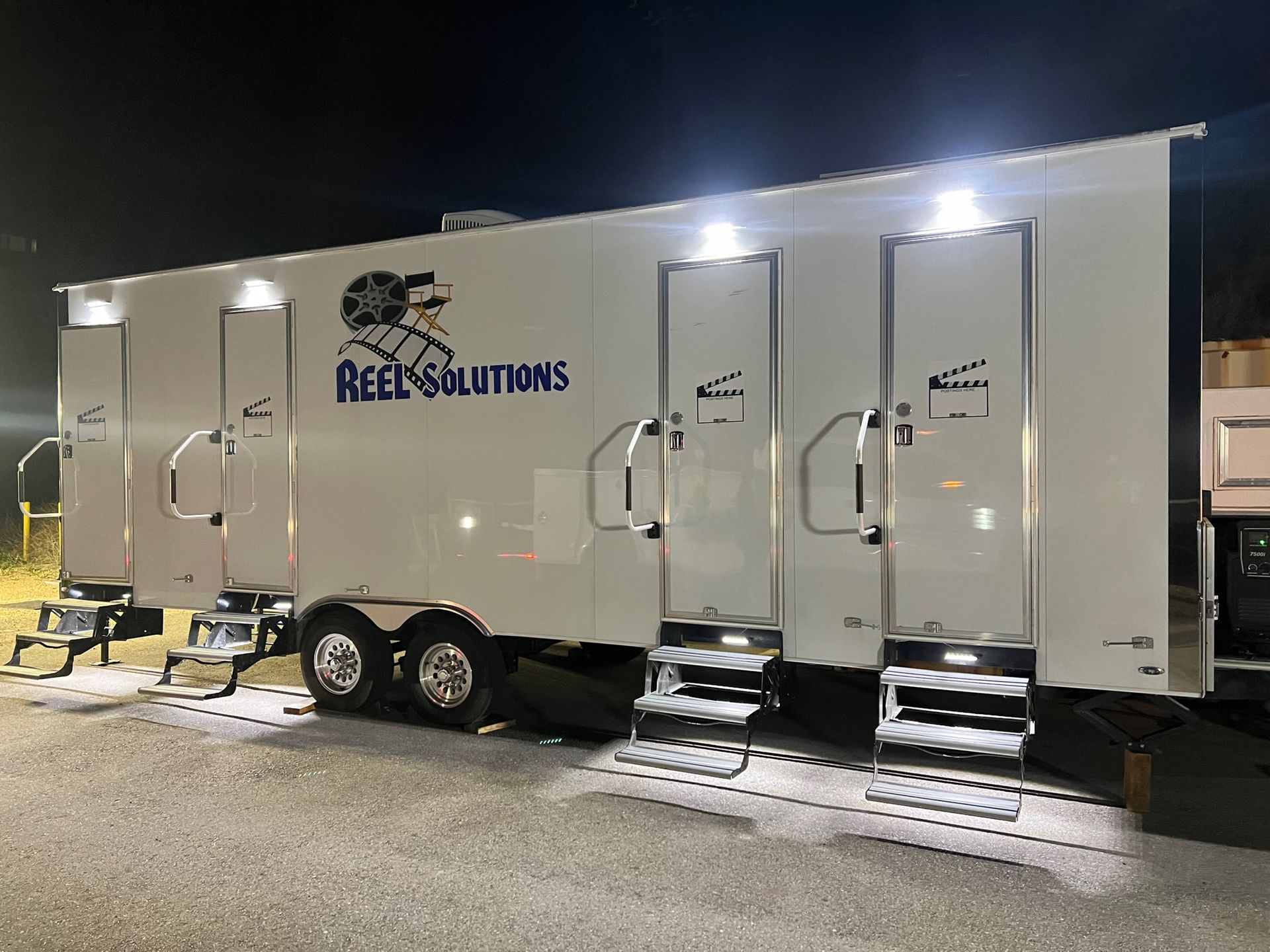 White portable restroom trailer with three stalls, lit up at night; 