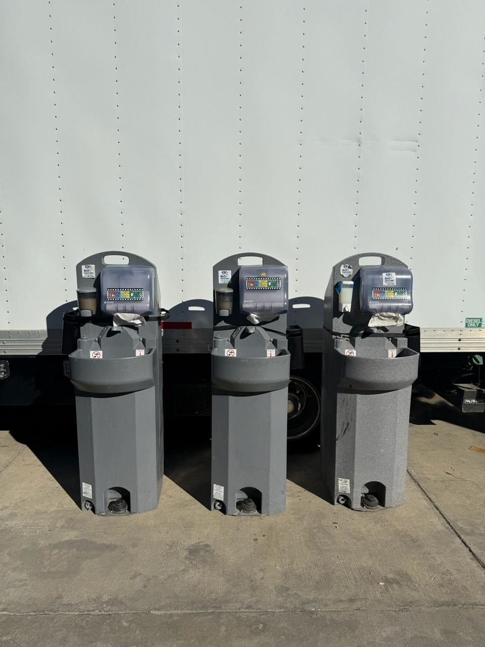 Three gray portable handwashing stations with sinks in front of a white truck.