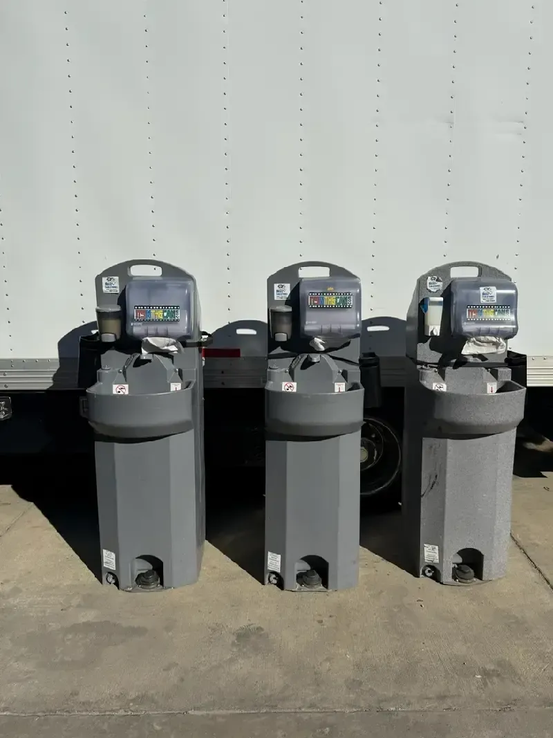 Three gray portable handwashing stations in front of a white truck.