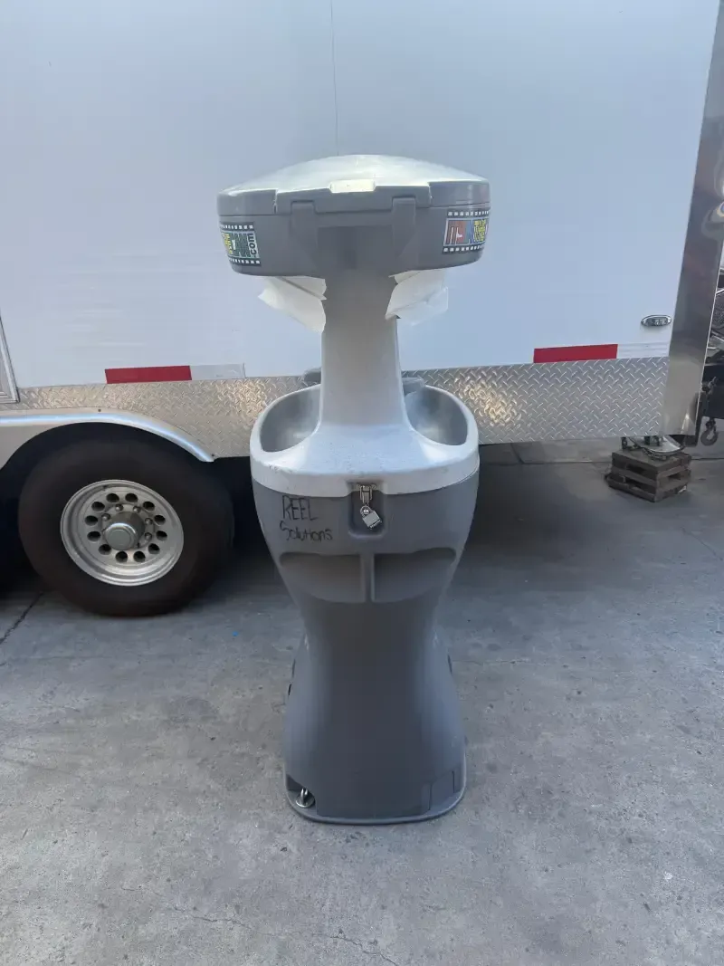 A portable handwashing station with gray and white plastic, outdoors.