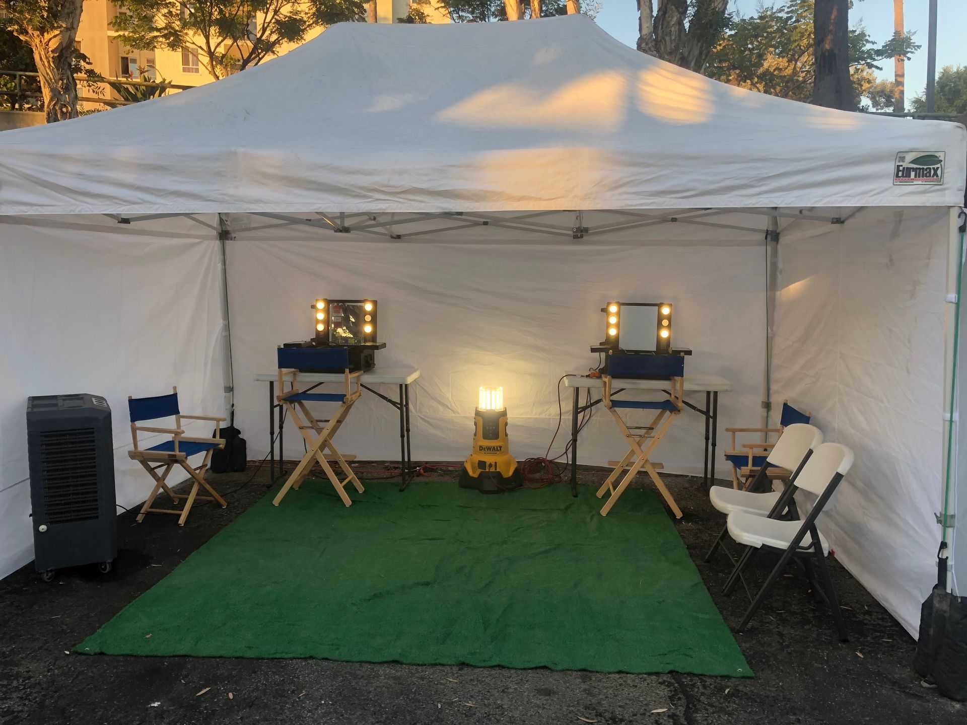 Inside a white tent: two makeup stations with mirrors, chairs, and a green mat.