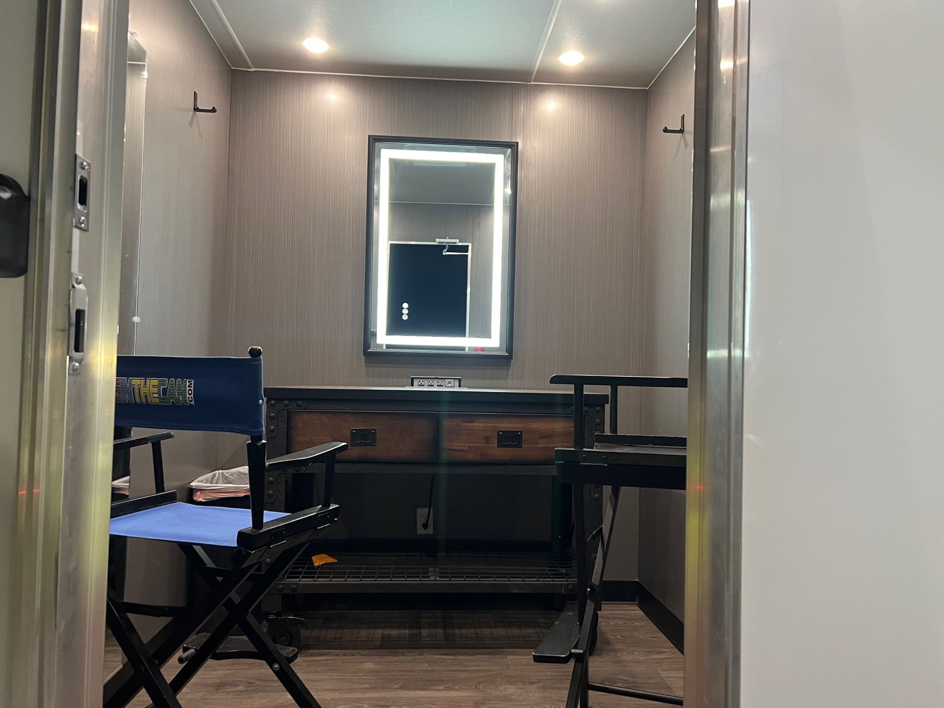 A makeup trailer interior with a lit mirror, vanity, and director's chair.