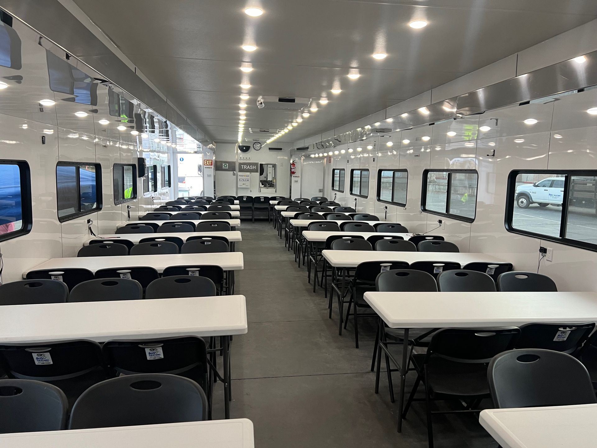 Interior of a large white mobile trailer with rows of tables and chairs, likely a temporary office or dining area.