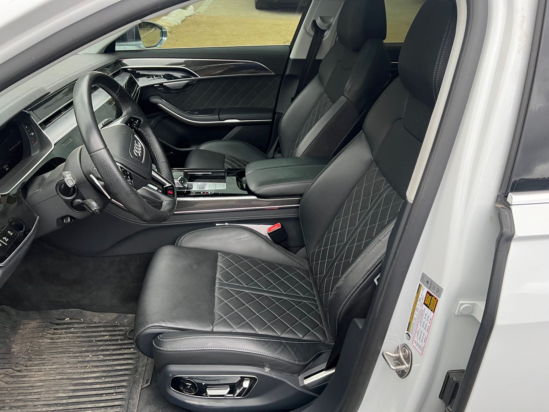 Car interior: black leather seats with diamond stitching, steering wheel, dark wood trim.