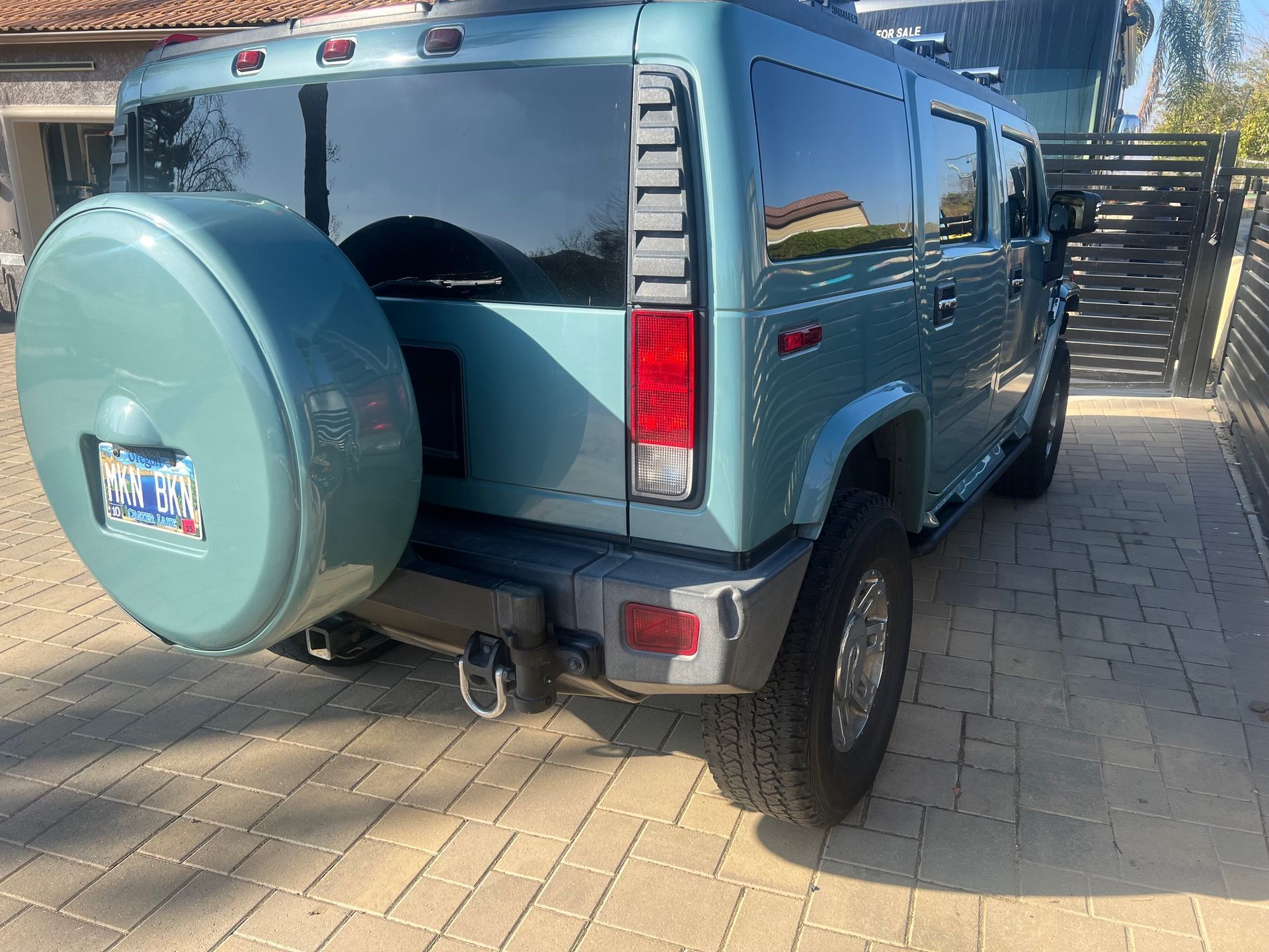 Teal Hummer H2 SUV parked on a paved driveway with a spare tire.