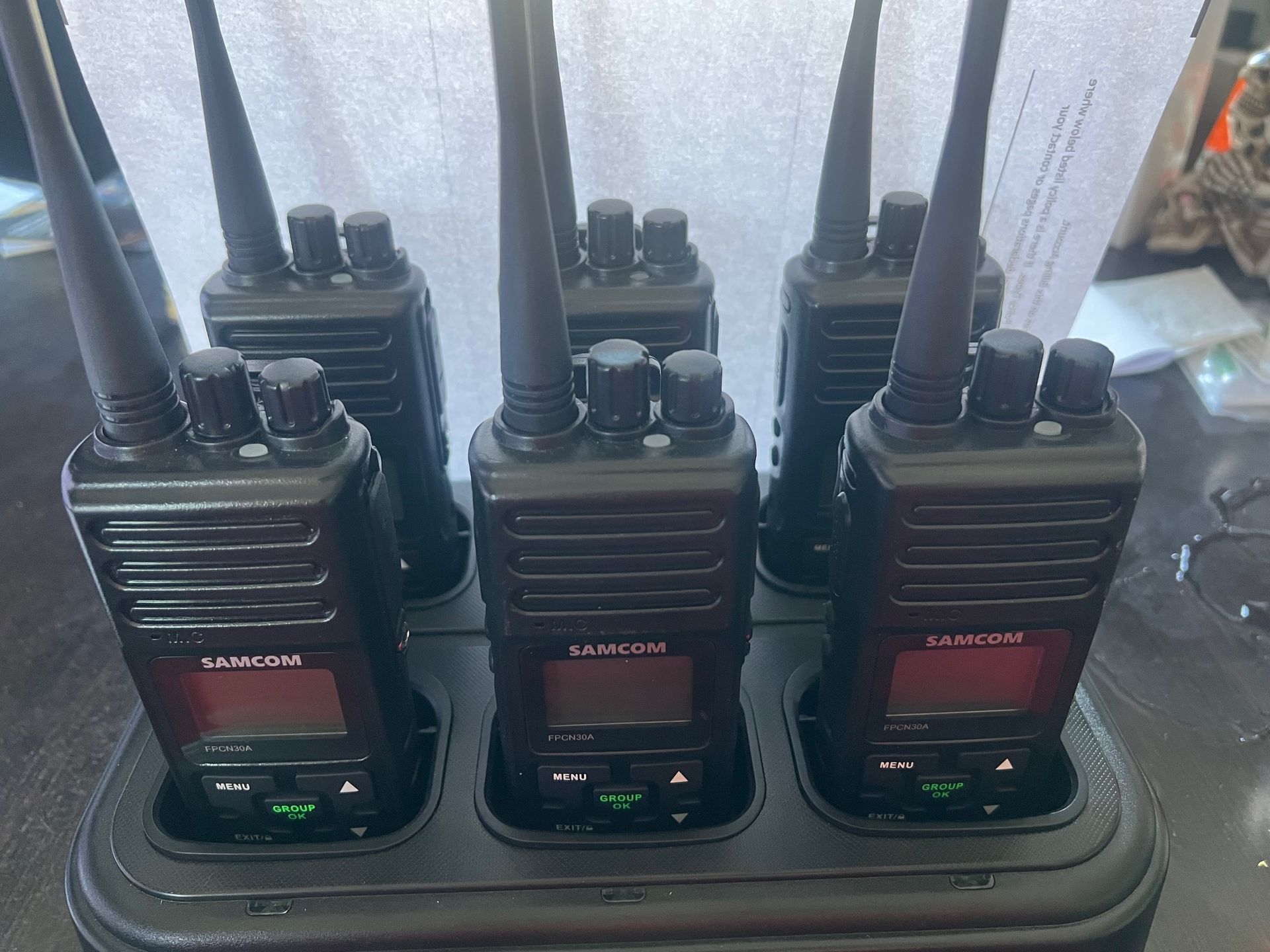 Six black two-way radios with antennas in a charging station, illuminated green.