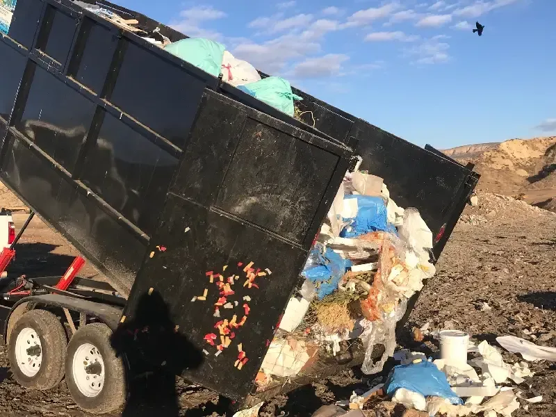 Dump truck dumping trash in a desert setting; black truck bed, blue sky.
