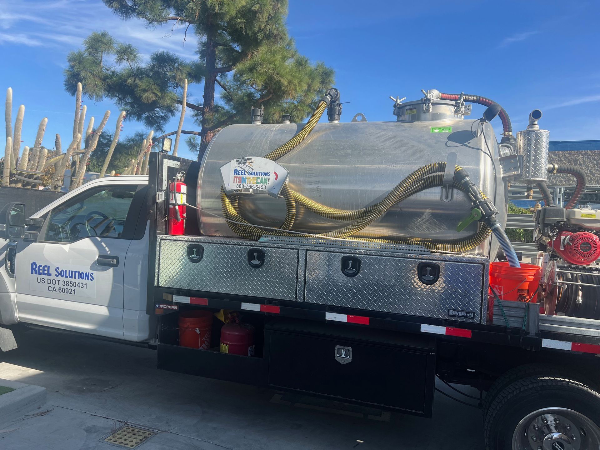 White truck with a silver tank on the bed, parked outside. A yellow hose extends from the tank.