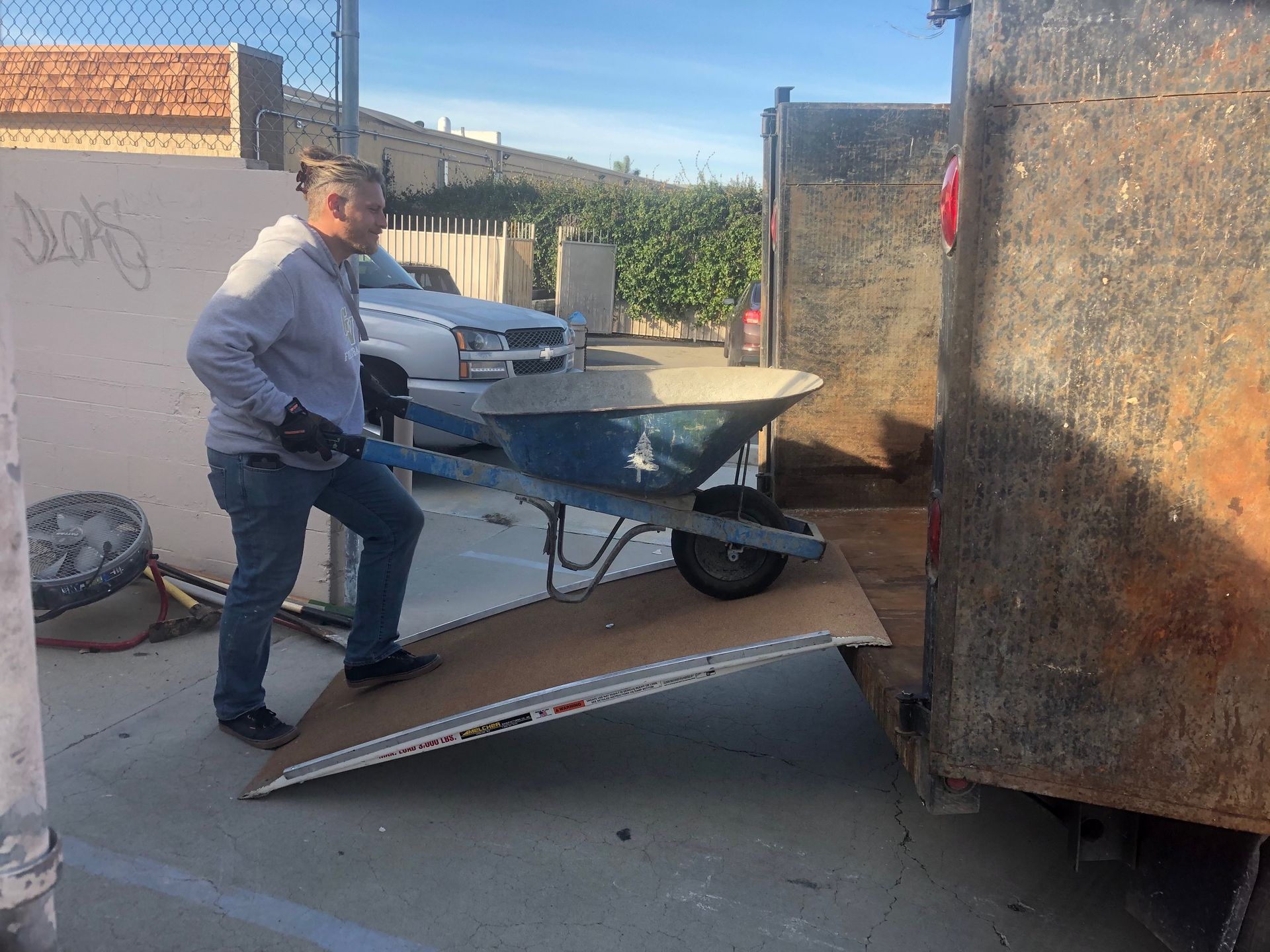Person pushing a blue wheelbarrow up a ramp into a truck.