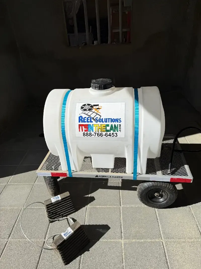 White water tank on a small wagon with black wheels, secured by blue straps.