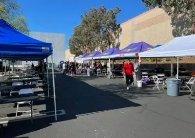 Outdoor event with tables under tents; people walking, blue sky background.