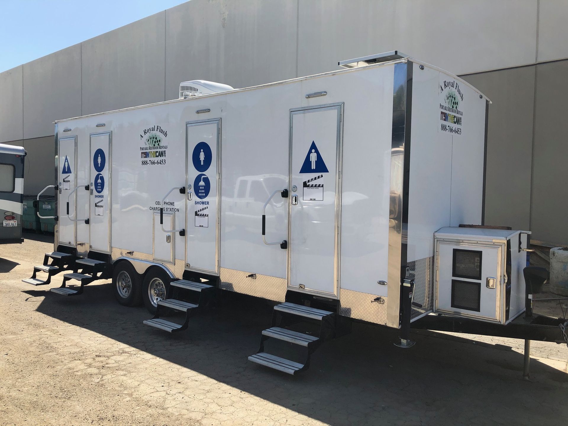White portable restroom trailer with multiple stalls, steps, and handrails.