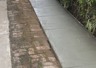 Newly poured concrete sidewalk next to a brick path and grassy area.