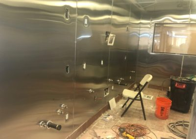 Interior room with stainless steel walls, electrical outlets, and a folding chair. Construction in progress.