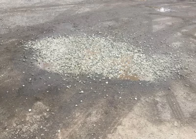 Puddle on pavement filled with gravel, likely to fill a pothole.