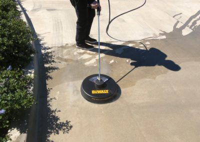 Person using a pressure washer with a circular head to clean a concrete surface outdoors.