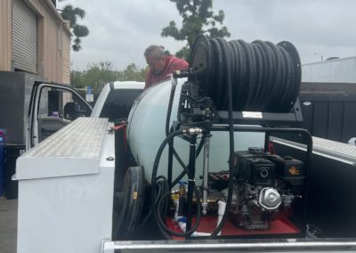 Man near a truck bed with a water tank and hose reel.