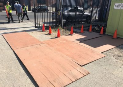 Plywood ramps and cones lead to a gate. Construction workers are visible nearby.