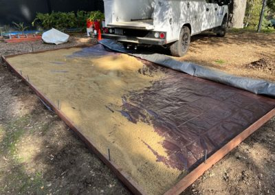 Sand spread within wooden frame, partially covered by tarp, with utility truck parked nearby.