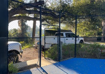 White trucks parked near a fence with an open gate; trees in the background, blue surface in the foreground.