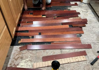 Person removing hardwood flooring from a kitchen, pieces scattered on the floor.