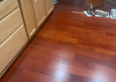 Reddish-brown hardwood floor next to light wood cabinets. Three stones sit on a paper.