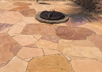 Flagstone patio with fire pit. Brown, tan, and reddish-purple stones, fire pit with black cover.