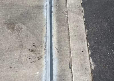 Concrete and asphalt surface with a narrow groove filled with sealant.