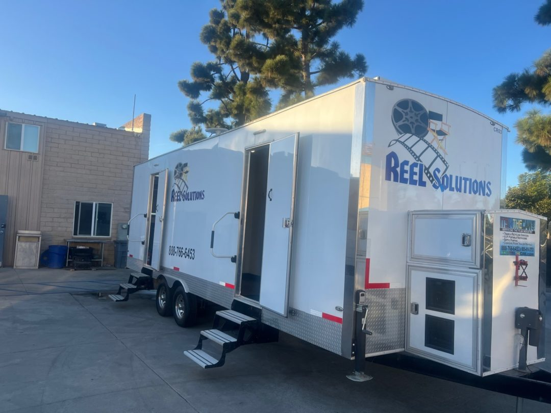 White trailer with Reel Solutions logo parked outdoors, featuring open doors and steps.