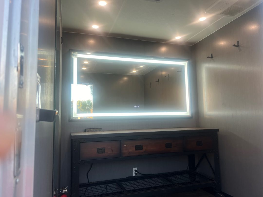 Bathroom with a lit rectangular mirror above a wooden vanity.