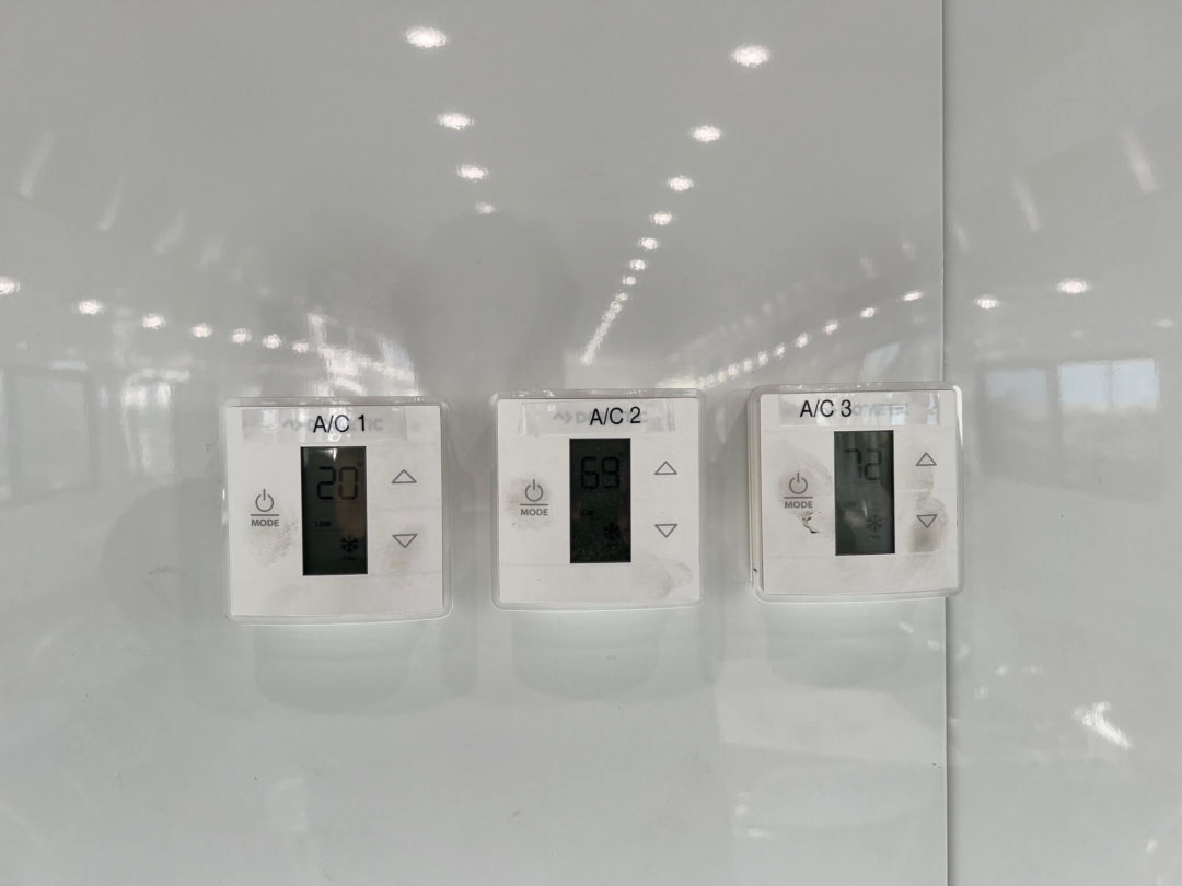 Three white thermostats mounted on a white wall, each with a digital display and buttons.