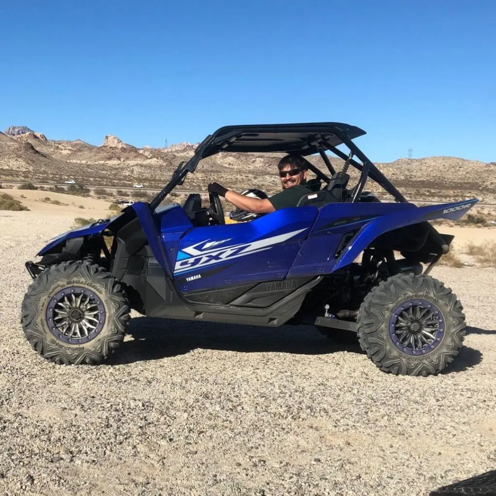 Man driving blue off-road vehicle in desert landscape under a clear blue sky.