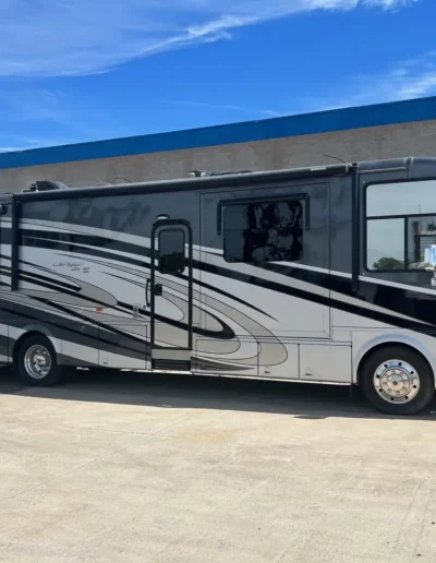 Gray and white RV parked in front of a blue-roofed building on a sunny day.