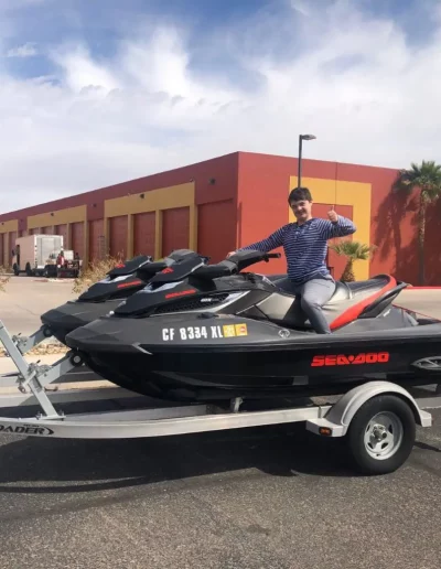 Man on jet ski on a trailer with warehouses in the background, making a hand gesture.