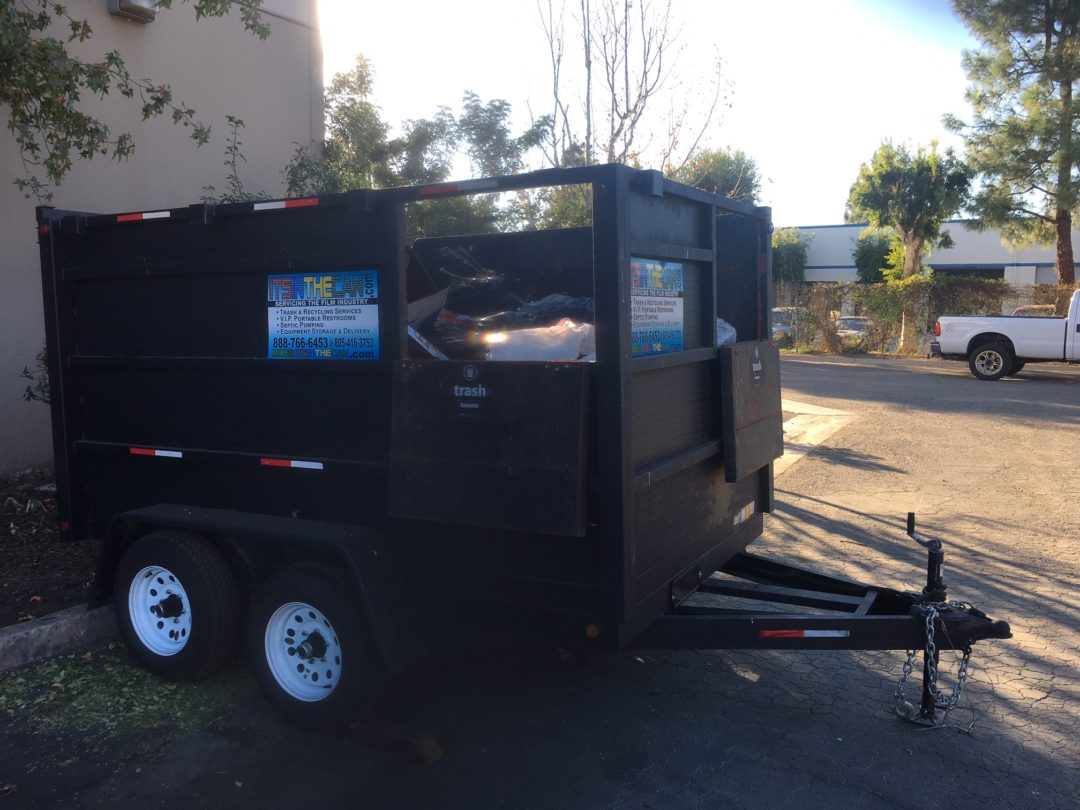 Black dumpster trailer with contents, parked outside.