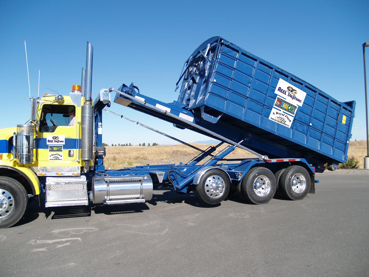 Blue dump truck with container raised, against a clear sky.