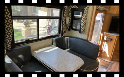 Interior of a camper with a table, seating, and windows. Black and white film border.