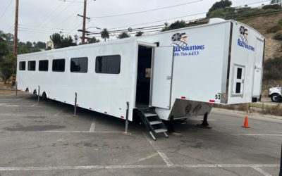 White mobile office trailer in a parking lot, door open with steps, company logo visible.