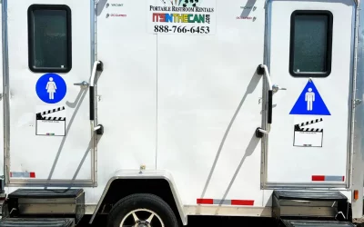 White trailer with two doors for portable restrooms, one marked for women and one for men.