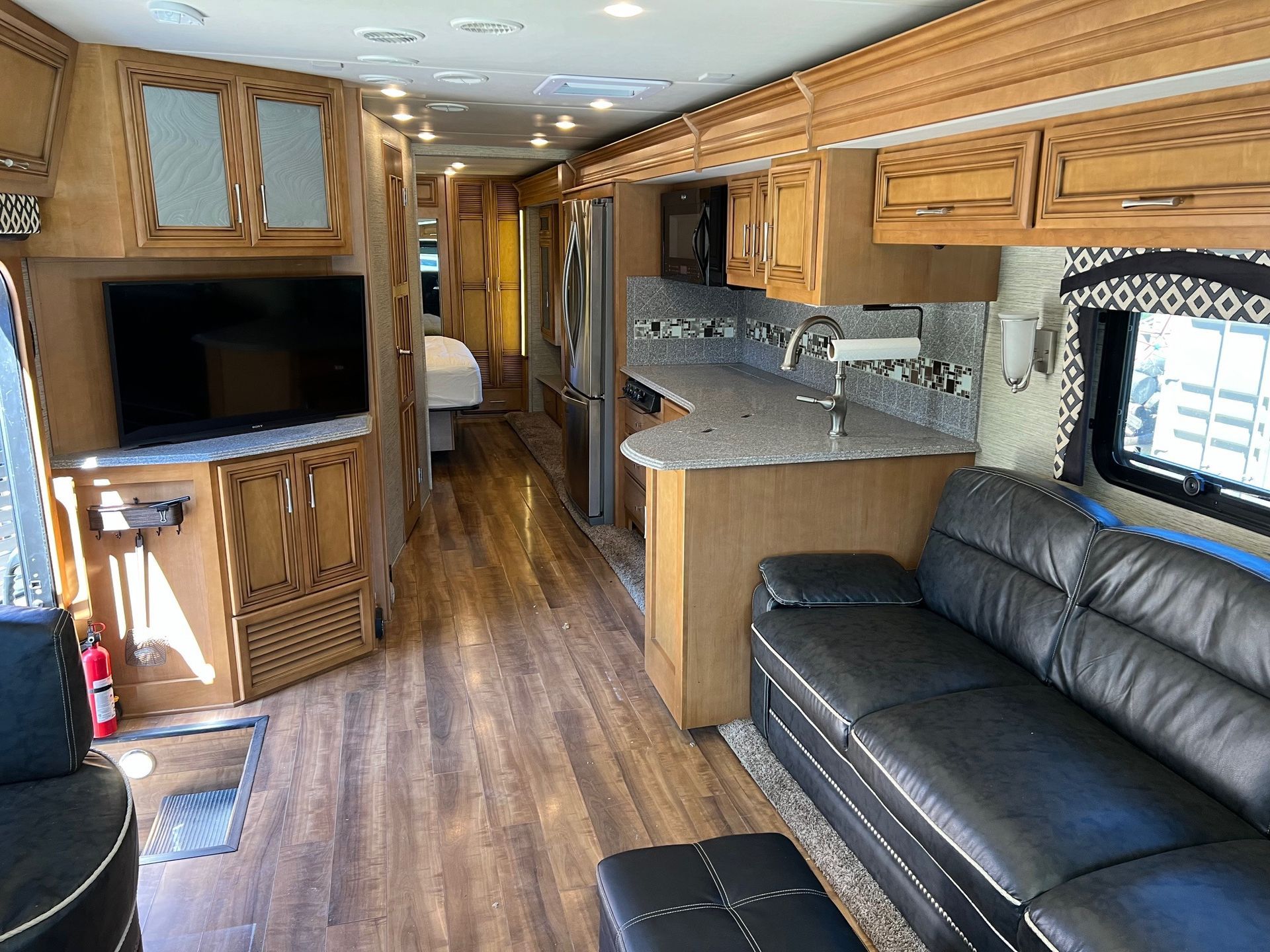 Interior view of a luxury RV with wood cabinetry, a black leather sofa, and a kitchen area.