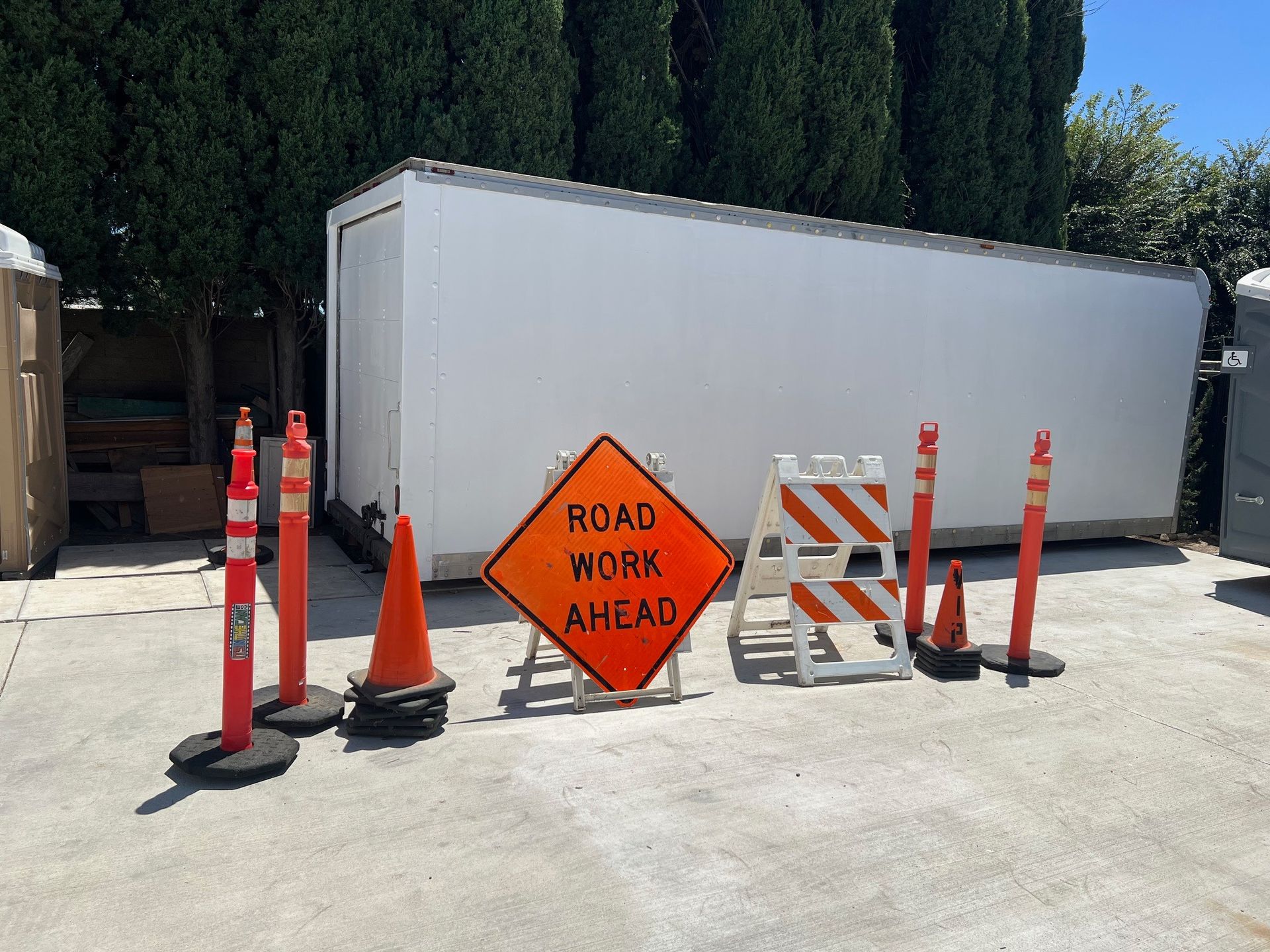Road work ahead sign, orange cones, and barricades in front of a white storage container.