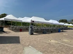 White canopies over rows of tables and chairs set up on a brick surface outdoors.