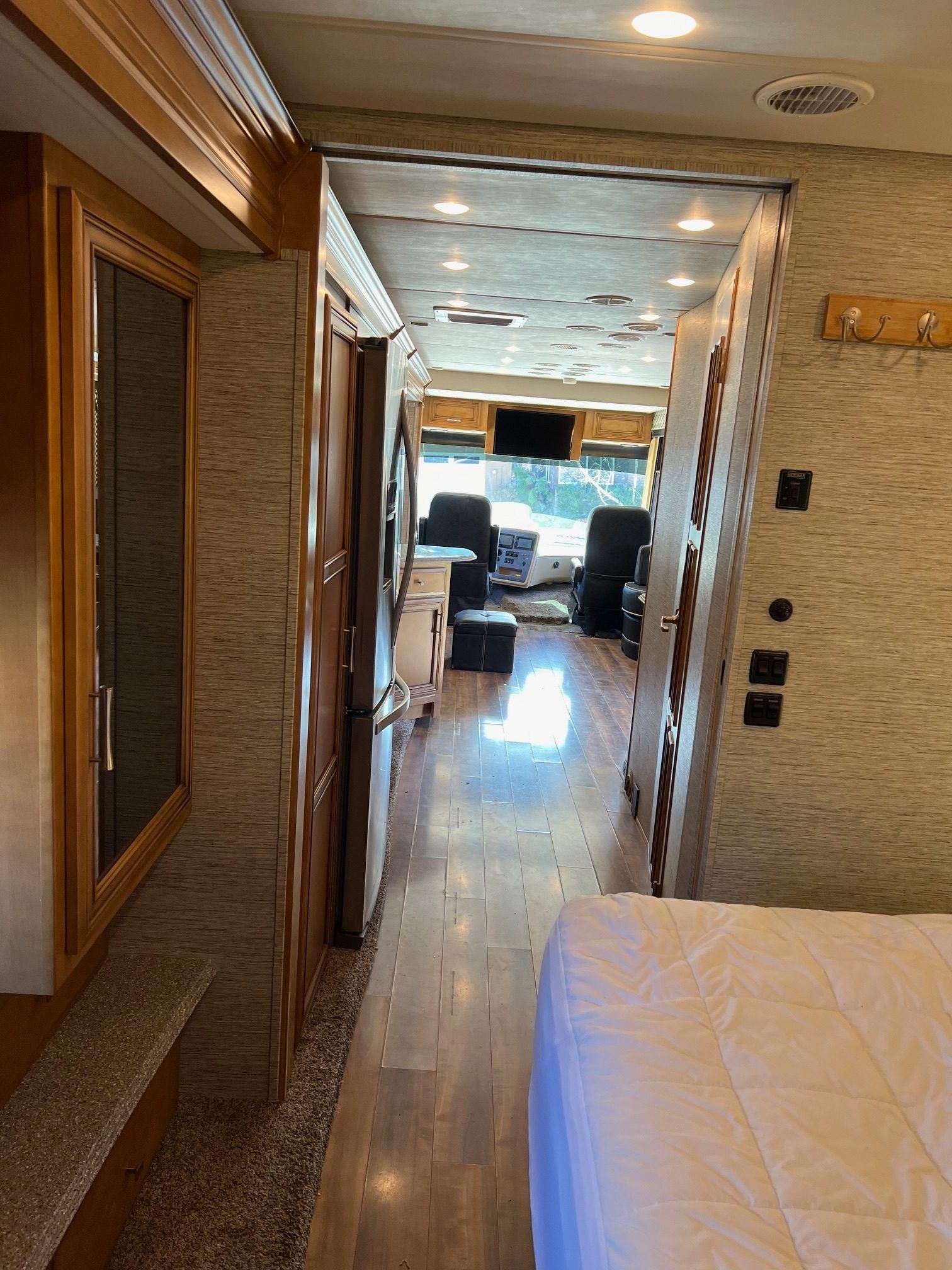Interior of a motorhome, looking down a narrow hallway towards the driver's area. Brown wood trim and neutral-toned walls.