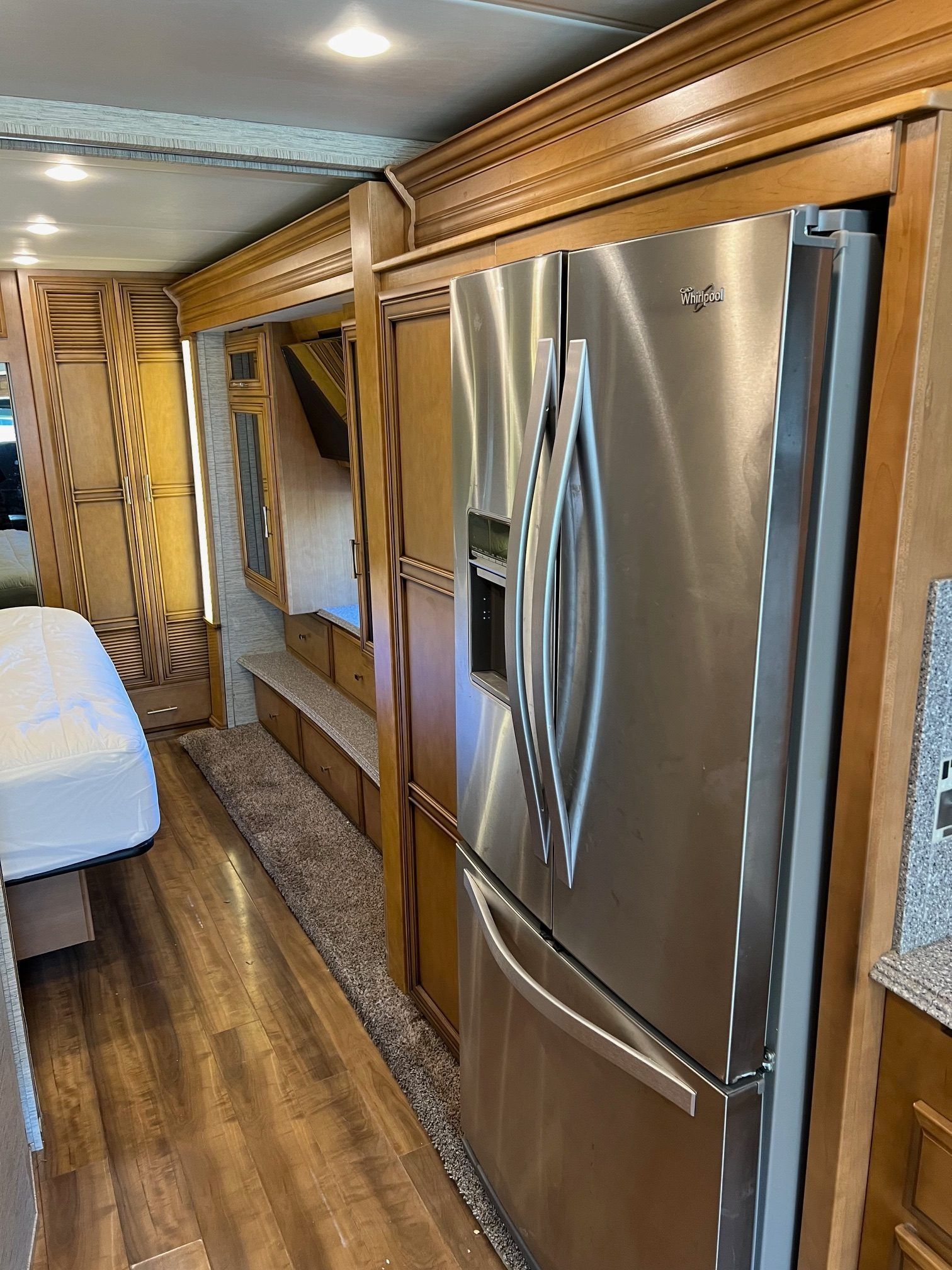 Interior of a recreational vehicle. Stainless steel refrigerator, wood paneling, and a bed are visible.