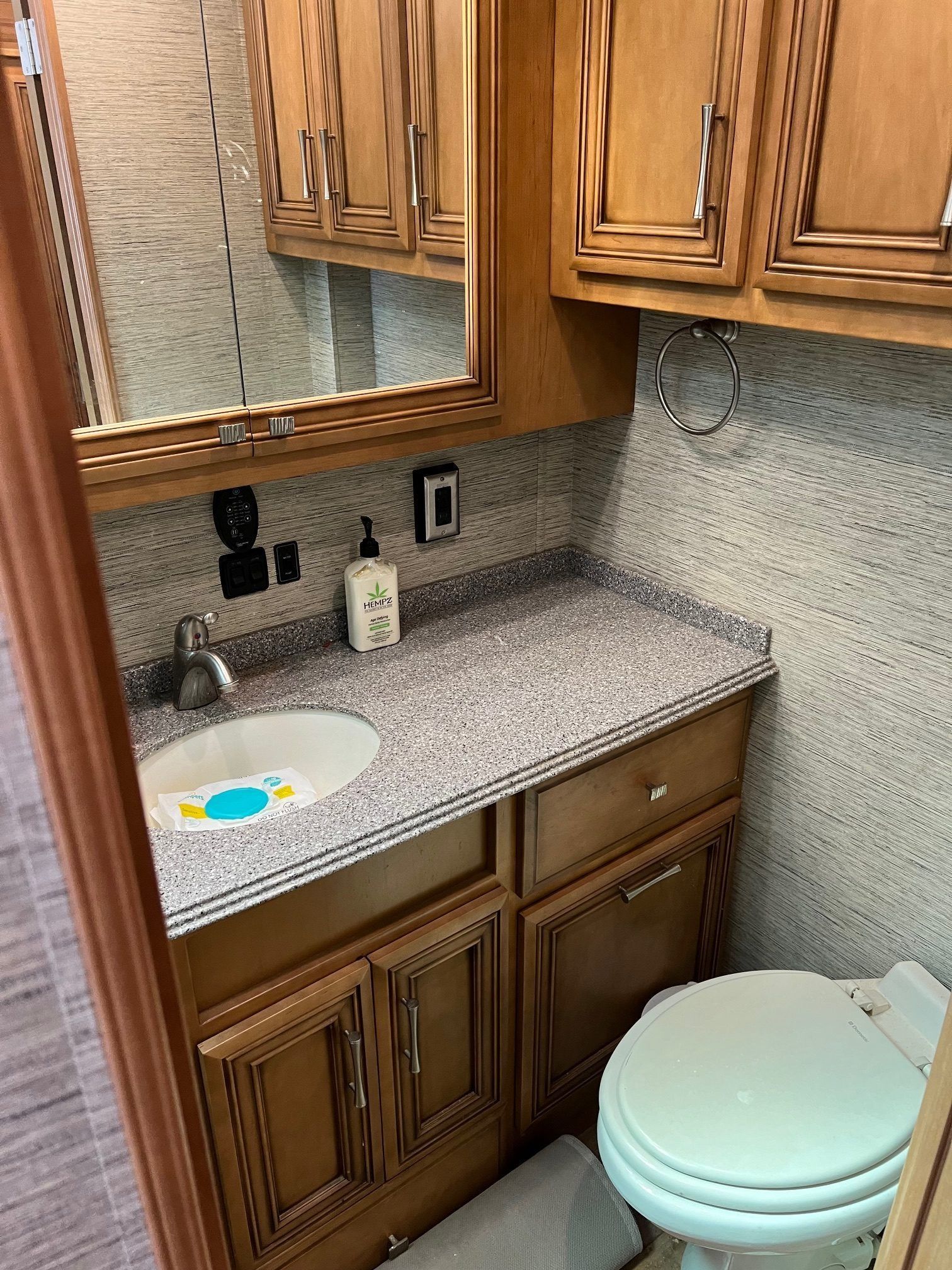 Bathroom in a recreational vehicle: sink, toilet, countertop, cabinets, and mirror. Beige and brown tones.