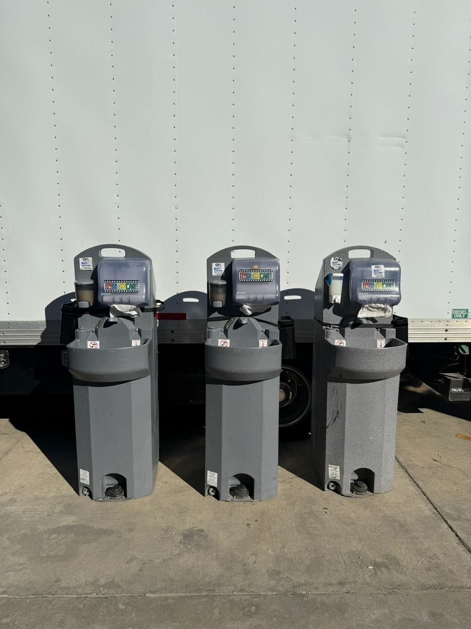 Three gray portable handwashing stations in front of a white truck.