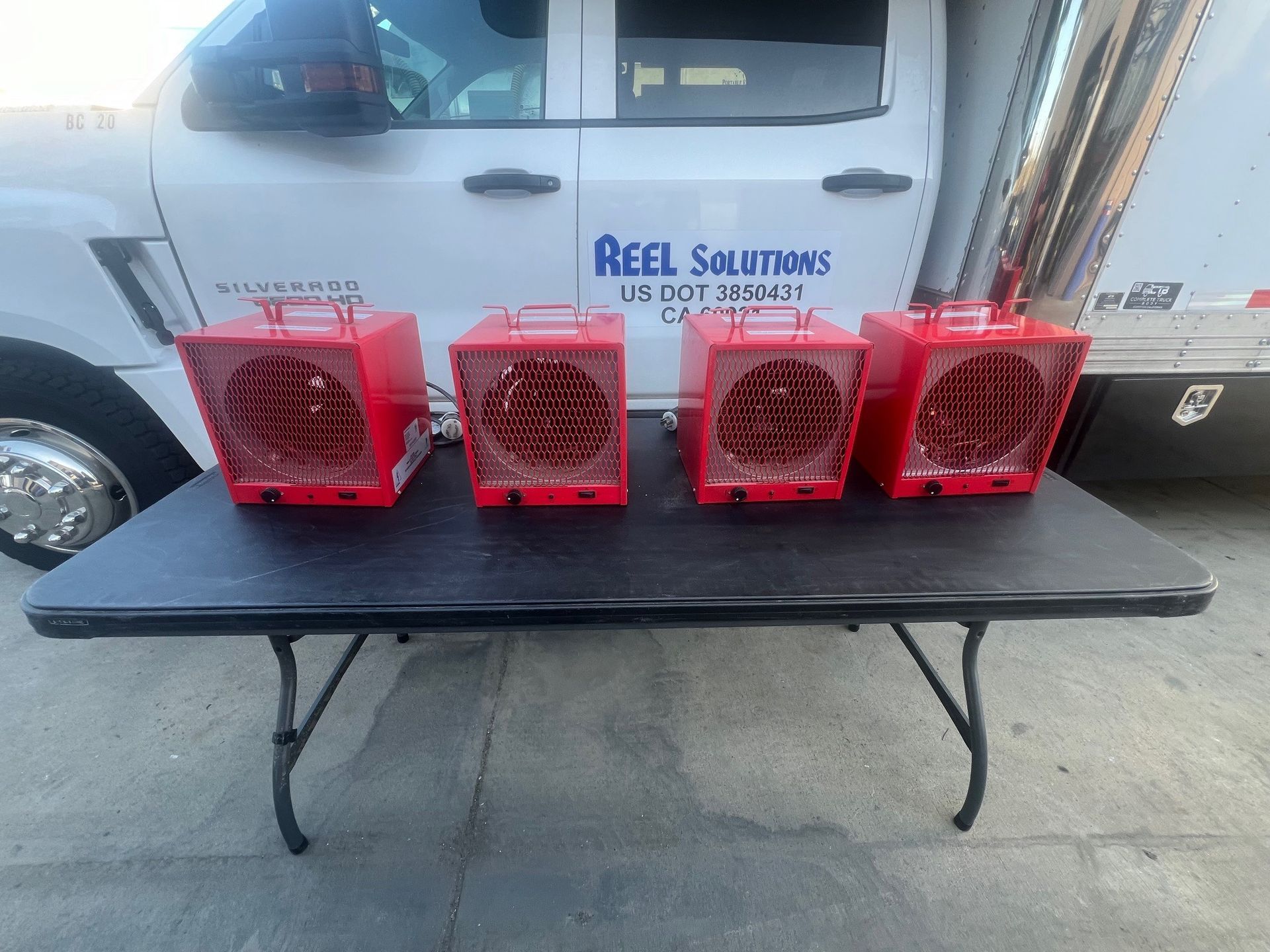 Four red heaters sit on a black table in front of a white truck.