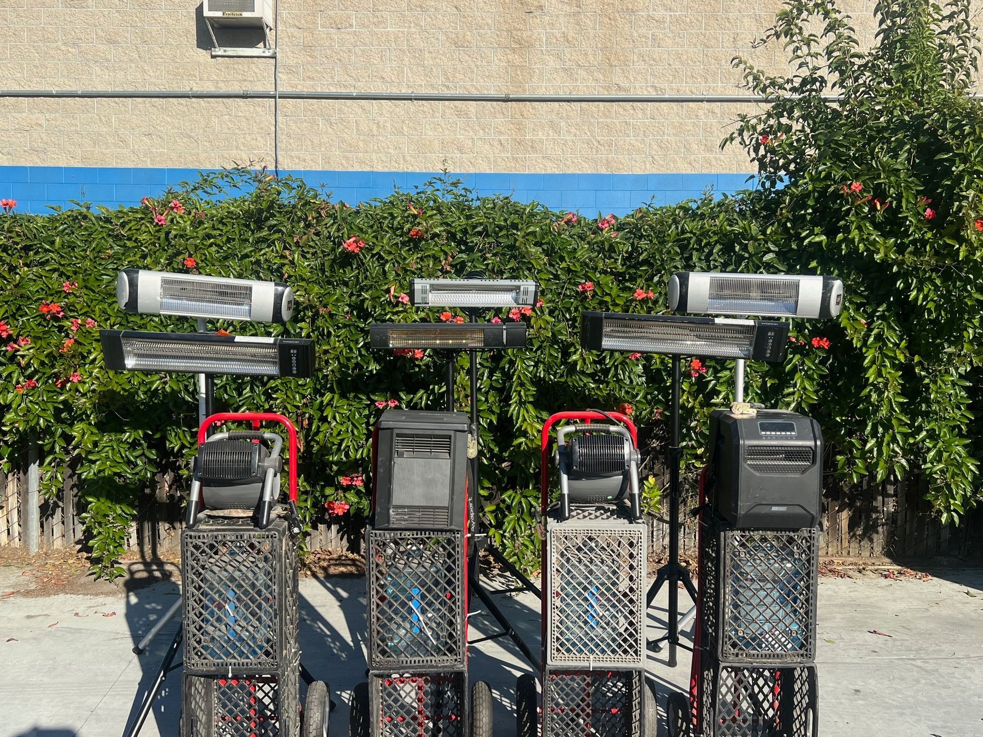 Three speakers and heaters mounted on crates, outdoors, in front of a green bush.