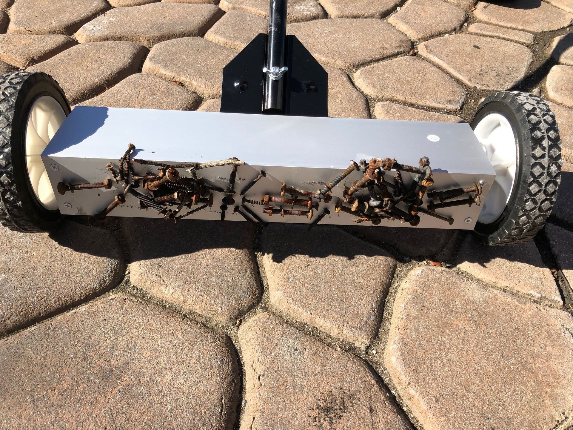 Magnetic sweeper collecting metal debris on a paved surface.